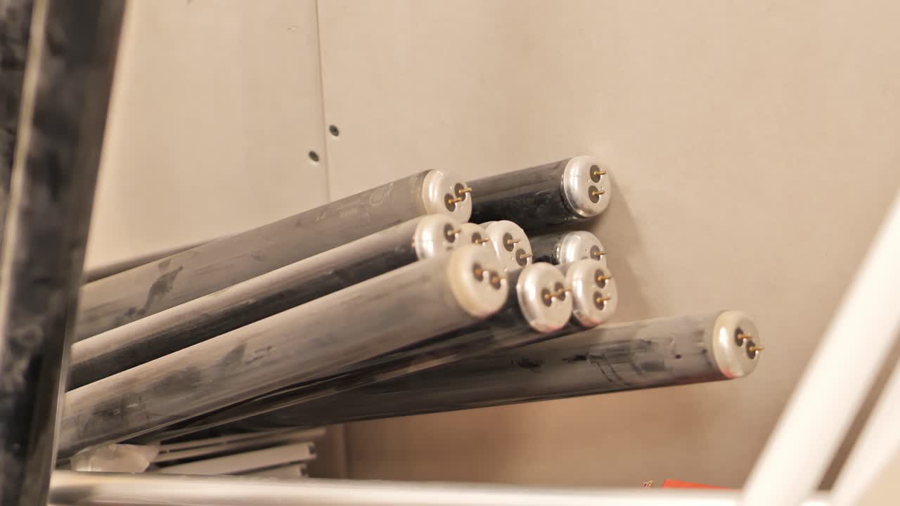Handheld camera panning left across fluorescent light tubes in storage room.