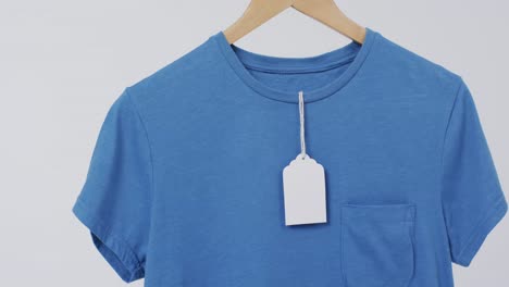 Video-of-blue-t-shirt-with-tag-on-hanger-and-copy-space-on-white-background