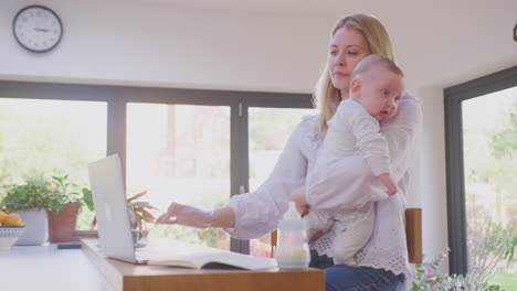 Madre-Trabajadora-Usando-Una-Computadora-Portátil-En-Casa-Mientras-Cuida-Y-Abraza-A-Su-Hijo,-Filmada-En-Cámara-Lenta