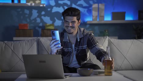 Young-man-video-chatting-on-the-phone-at-night,-drinking-alcohol.