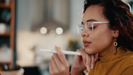 young woman in glasses looking at a pen while sitting at a desk