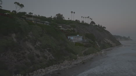 Slow-aerial-dolly-toward-a-seafront-apartment-with-waves-crashing-against-the-shore