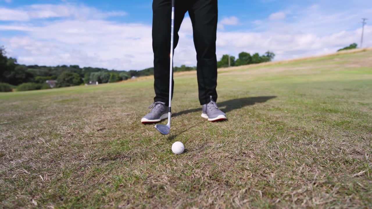 Golfer entering frame, swinging short, partner placing ball, digits orbiting ball feet preparing