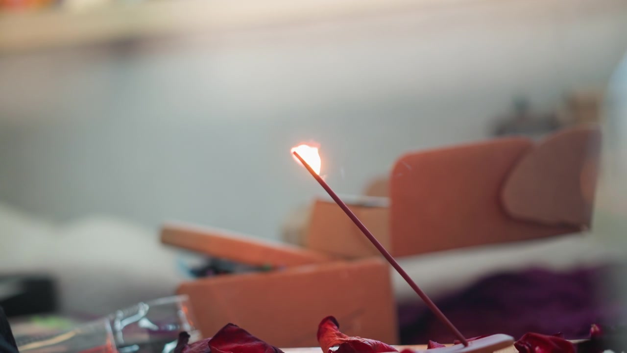 Bastoncino d'incenso che brucia su un altare, primo piano della fiamma e del fumo che si disperde, sfondo bokeh caldo e accogliente, praticante che lo accende per divinazione e meditazione tranquille, brace e cenere che covano lentamente.