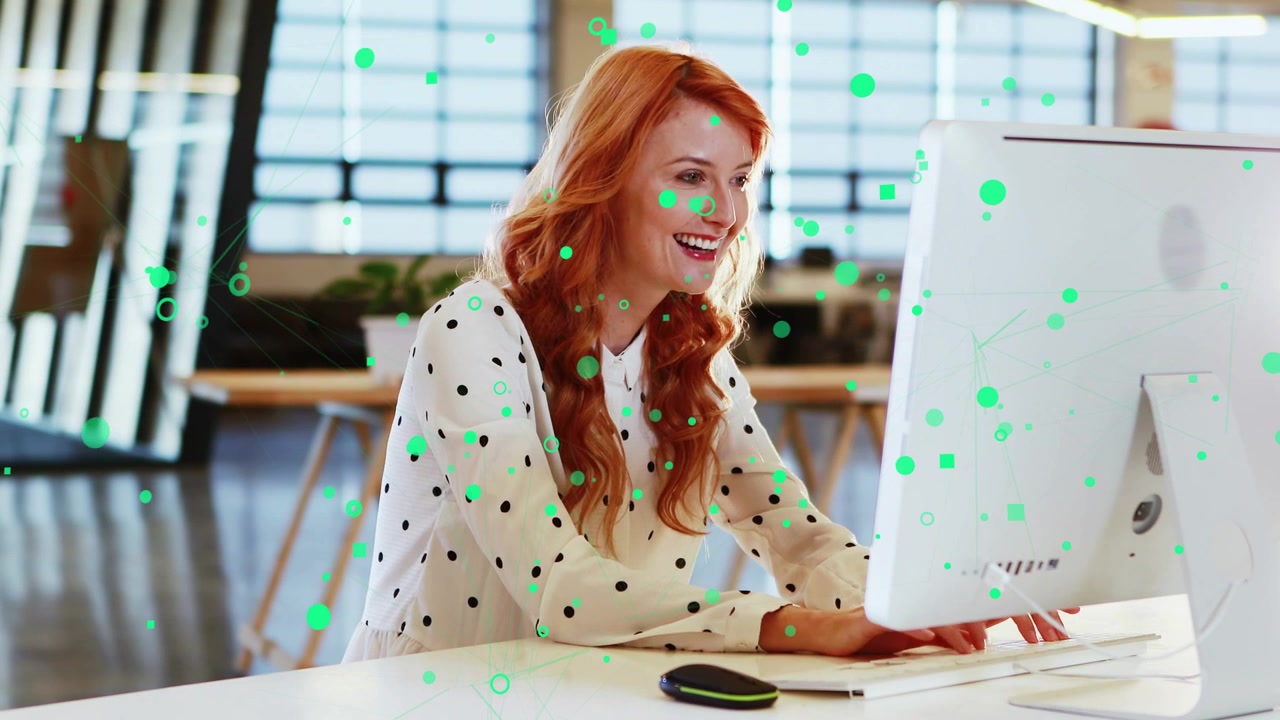 Donna che appoggia il mento, posiziona il mouse, clicca e digita, con particelle verdi che appaiono sullo schermo, mentre sorride esaminando la tecnologia.
