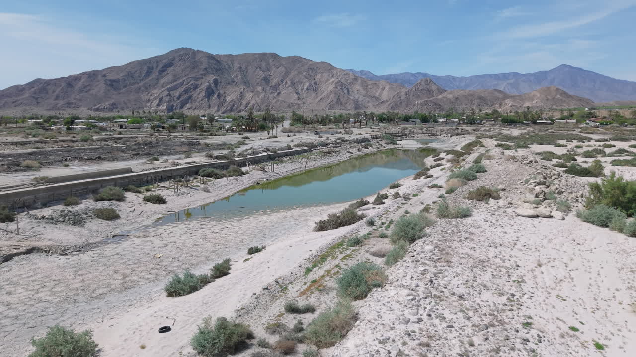Low drone shot arcing left to right over the marina basin at Desert Shores, California with stagnant water remaining in the channel. The San Jacinto Mountains rise in the background