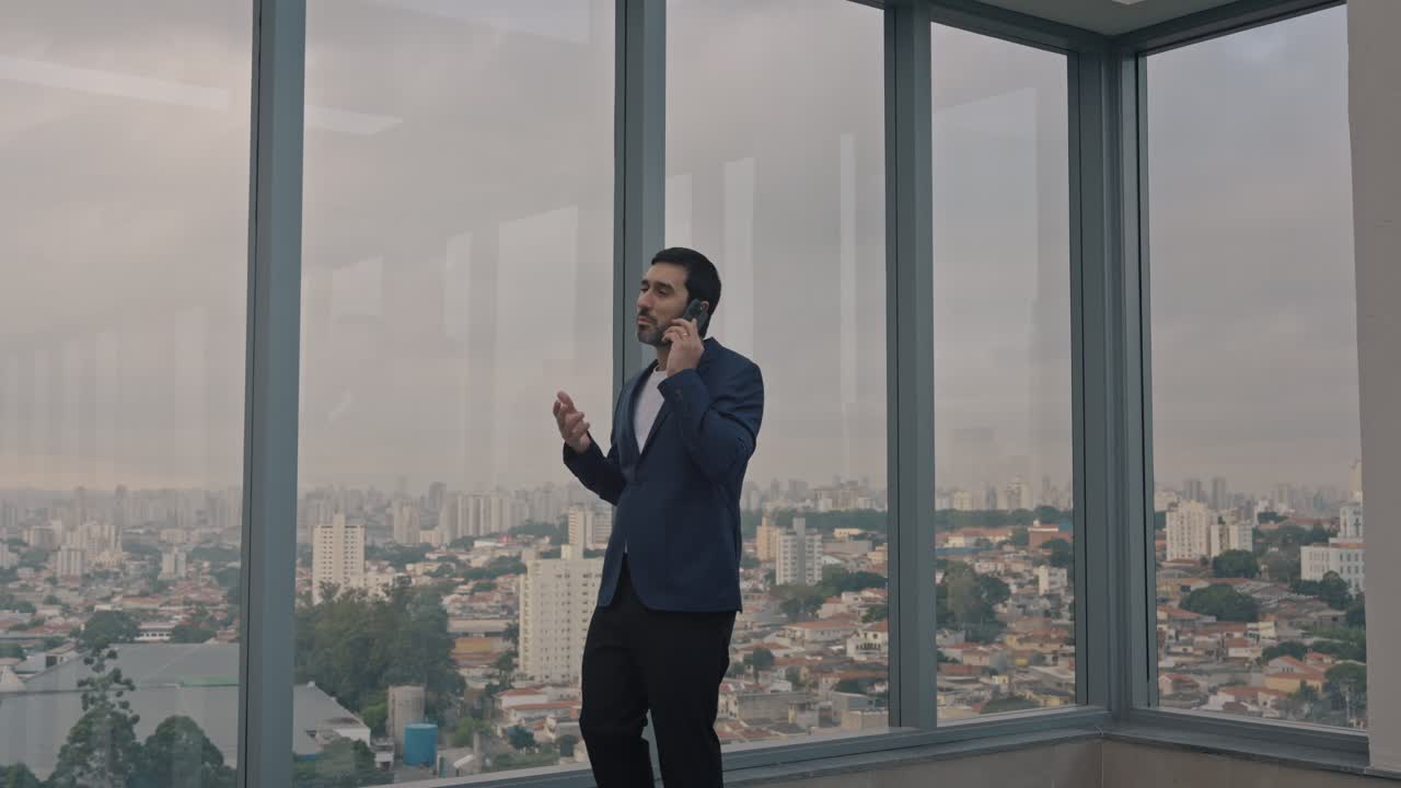 Executive man walking and talking on the phone on the terrace of a modern building. Camera follows the man.