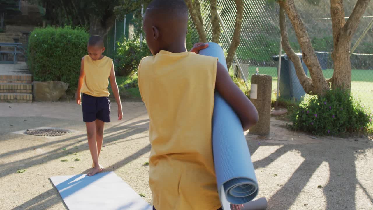 Due scolari afroamericani che raccolgono i tappetini dopo la lezione di yoga all'aperto.