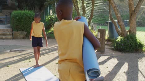Two-african-american-schoolboys-collecting-mats-after-oga-lesson-outdoors