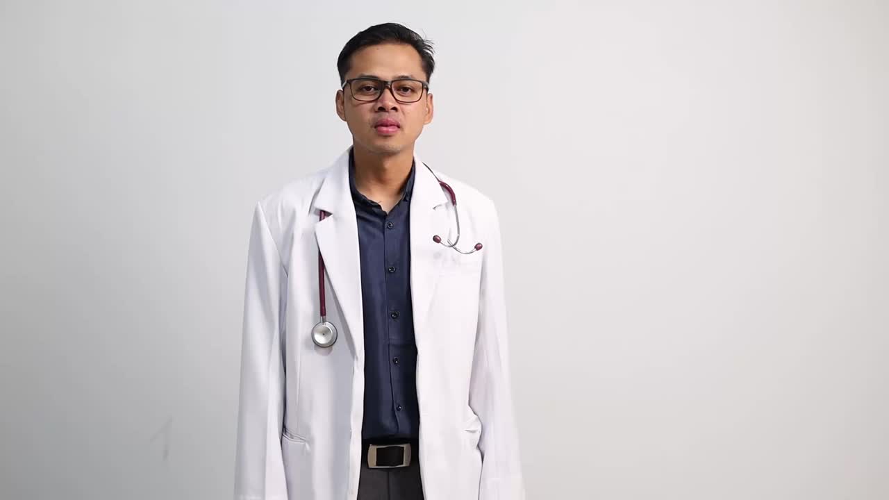 Seorang dokter pria Asia yang bahagia bertepuk tangan memberi selamat atau menyetujui dengan latar belakang abu-abu. Gestur salam atau perayaan