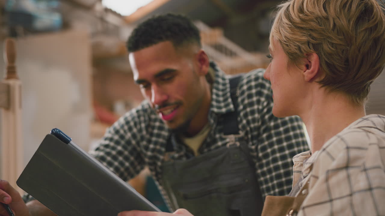 Male And Female Apprentices With Digital Tablet Working As Carpenters In Furniture Workshop