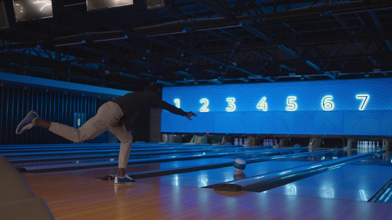 A black man bowling man throws a ball in slow motion and knocks down skittles. Play bowling. Throw balls on the floor of the bowling club