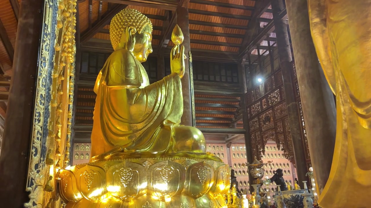 Cảnh bên trong Chùa Bái Đính ở Ninh Bình, Việt Nam, với tượng Phật vàng lớn cầm hoa sen bên trong chánh điện bằng gỗ được trang trí công phu.
