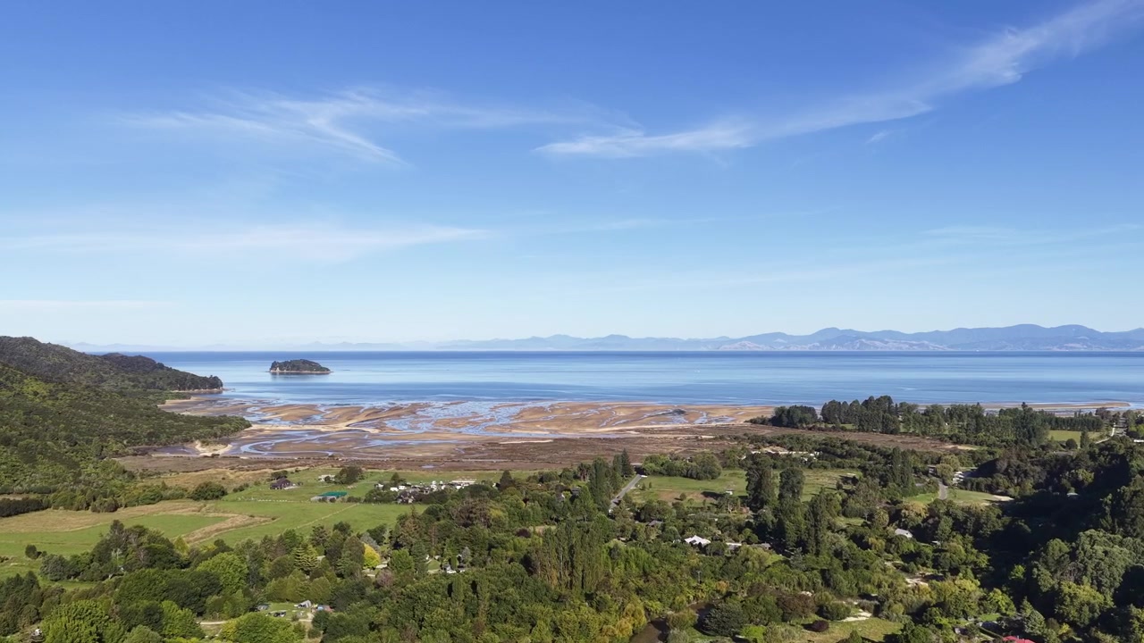 Droneopptak som avslører et fredelig kystlandskap med tidevannsflater, skog og hav på New Zealands Sørøy.
