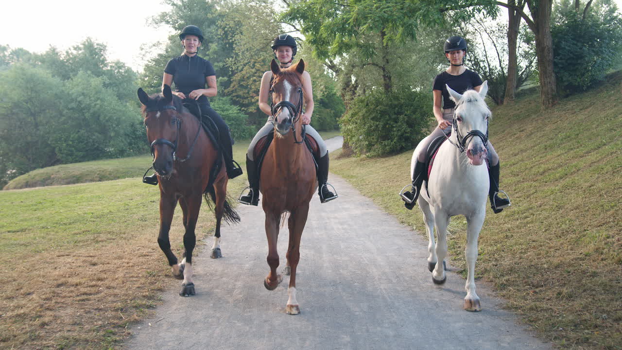 tres jinetes femeninos montando caballos a lo largo del sendero junto al río, vista frontal