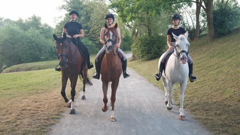 three female riders riding horses along the trail by the river, front view