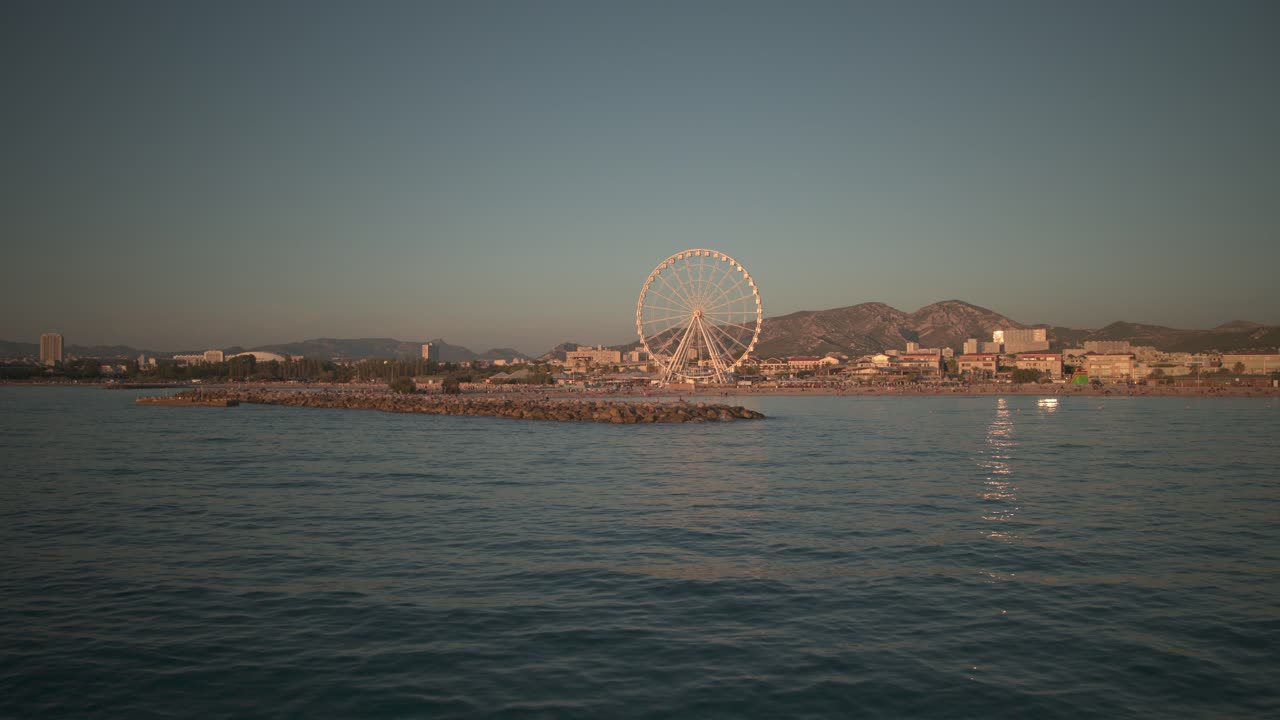 Static shot above the sea with a ferris wheel in background
Marseille in golden hour