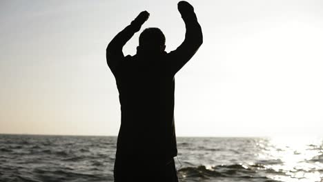 male figure standing before the sun stretching, twisting hands and body as a part of morning exercise routine. sportand fitness. wellbeing and healthcare