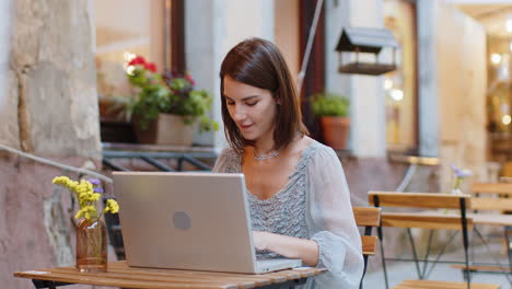 Woman-working-online-distant-job-with-laptop-in-city-cafe-or-restaurant-browsing-website-chatting