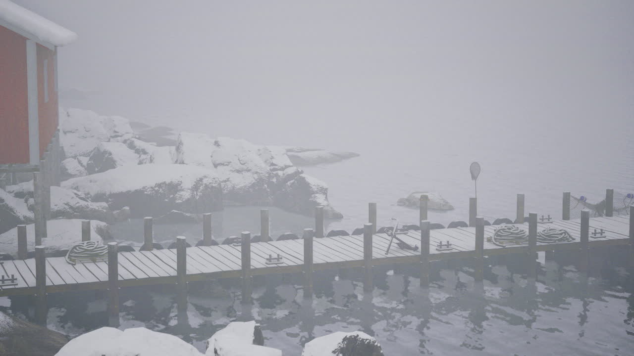 Misty winter harbor with a snowy dock and rocky shores surrounded by fog