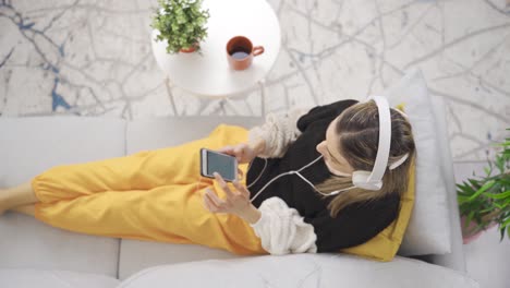 woman sitting on sofa at home listening to music with headphones.