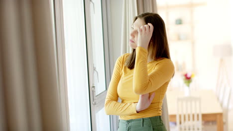 thoughtful caucasian woman looking through window at home, in slow motion