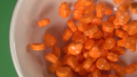 Primer-Plano-De-Calaveras-Naranjas-Y-Caramelos-Con-Forma-De-Huesos-Que-Caen-Sobre-Un-Plato,-Sobre-Un-Fondo-Cromático