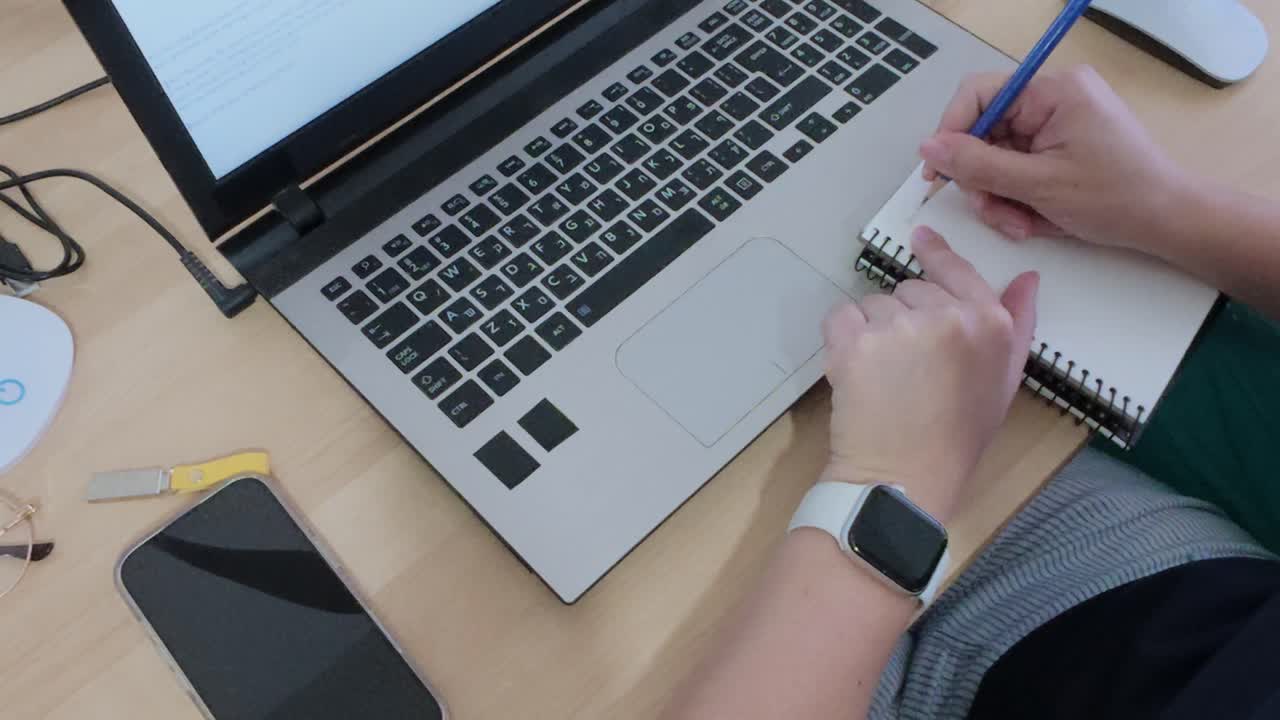 Student taking handwritten notes in a notebook during an online class or study session with a laptop