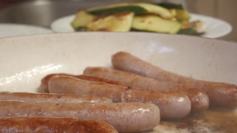 grilling sausages in a pan with a fork in action, with grilled zucchini in the background