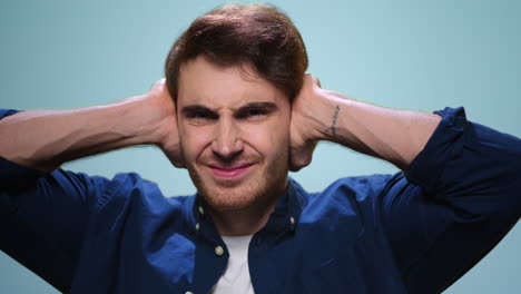 Stressed-man-shutting-ears-with-hands.-Worried-guy-grimacing-on-blue-background