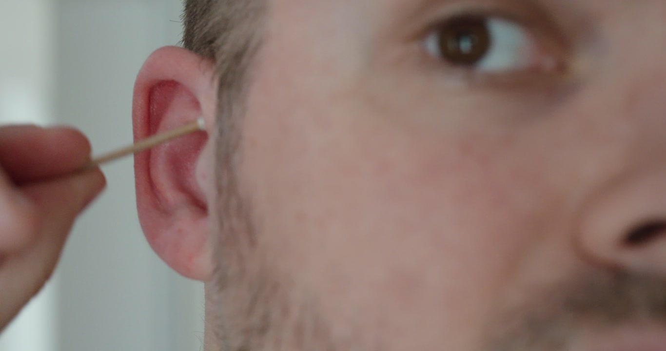Close-up of a man cleaning the outer ear with a cotton swab. Concept of hygiene, personal care and ear cleaning safety.