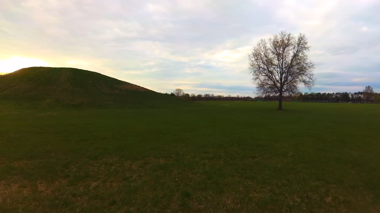 Walking in a grass field, with a view of a sunset and a large hill
