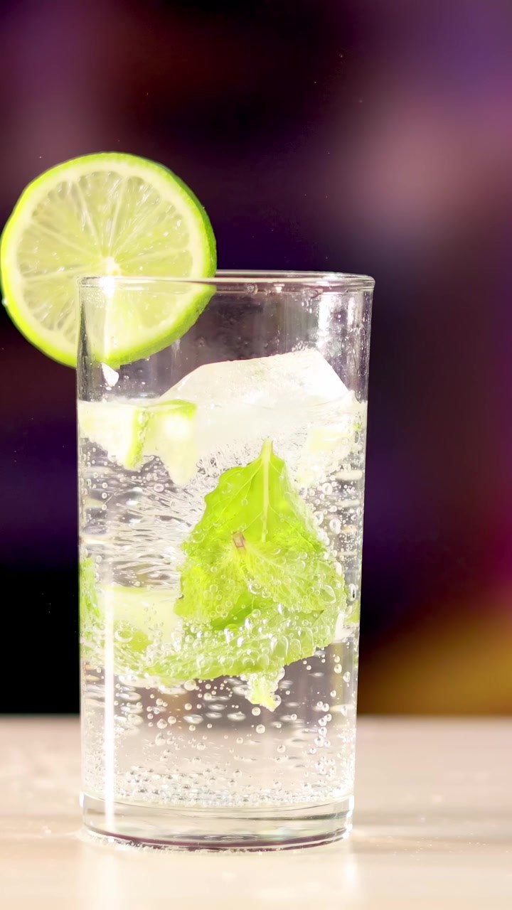 Un cocktail mojito con lime e menta su una superficie di legno, su uno sfondo sfocato e colorato.