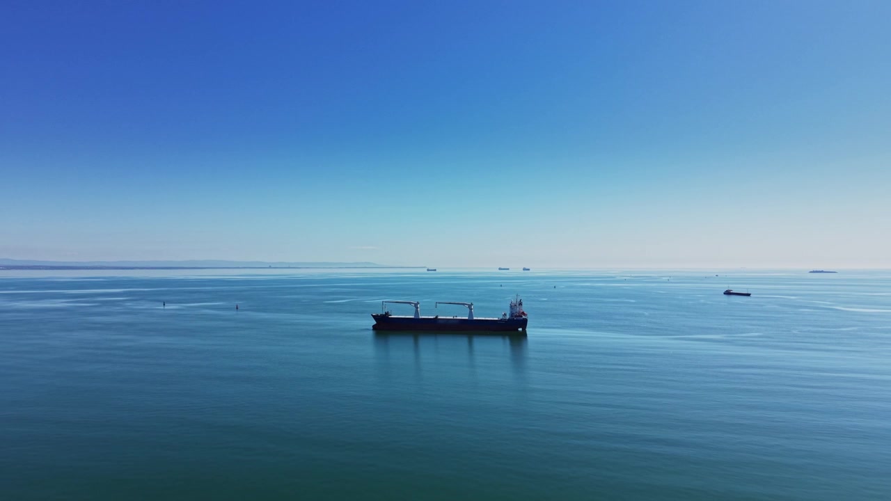 澄み切った青空の下、穏やかな水面を進む大型貨物船。