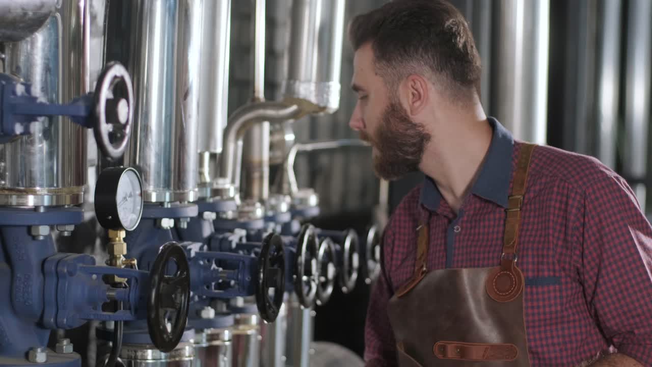 un joven cervecero con un delantal de cuero supervisa el proceso de fermentación de la cerveza en una fábrica de cerveza moderna