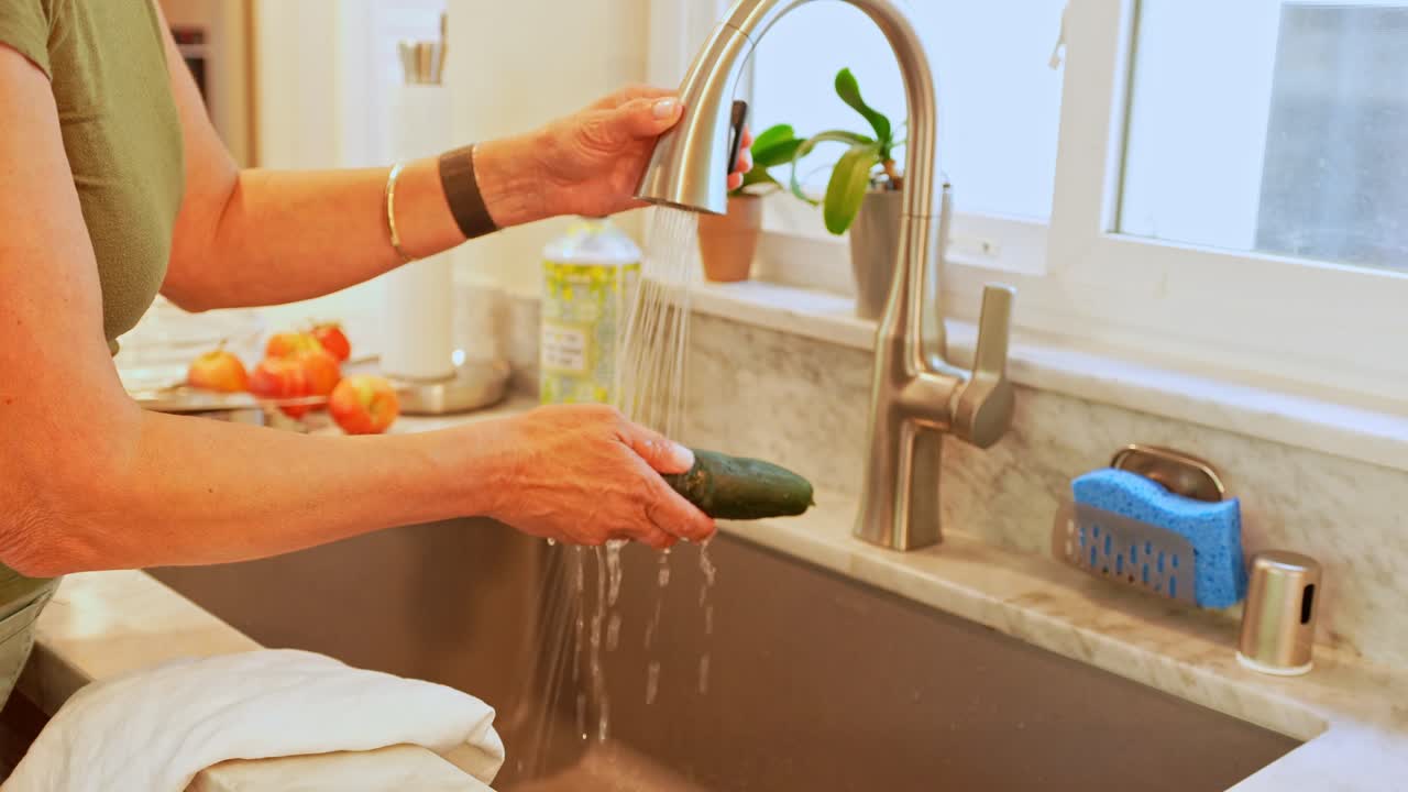 Woman Washing Cucumber in Kitchen Sink