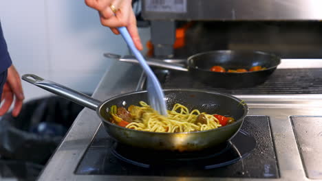 cooking and stirring the spaghetti with red tomatoes and mushrooms in the frying pan. video from a side.
