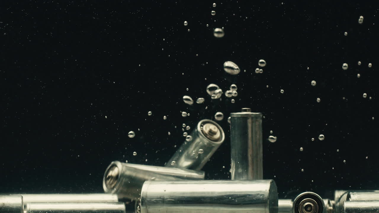 Silver batteries AA and AAA falling into water close-up. Double-A battery is a standard size single cell cylindrical dry battery. Batteries are common in portable electronic devices. Environmental impacts of lithium-ion batteries concept. An AA battery is composed of a single electrochemical cell th