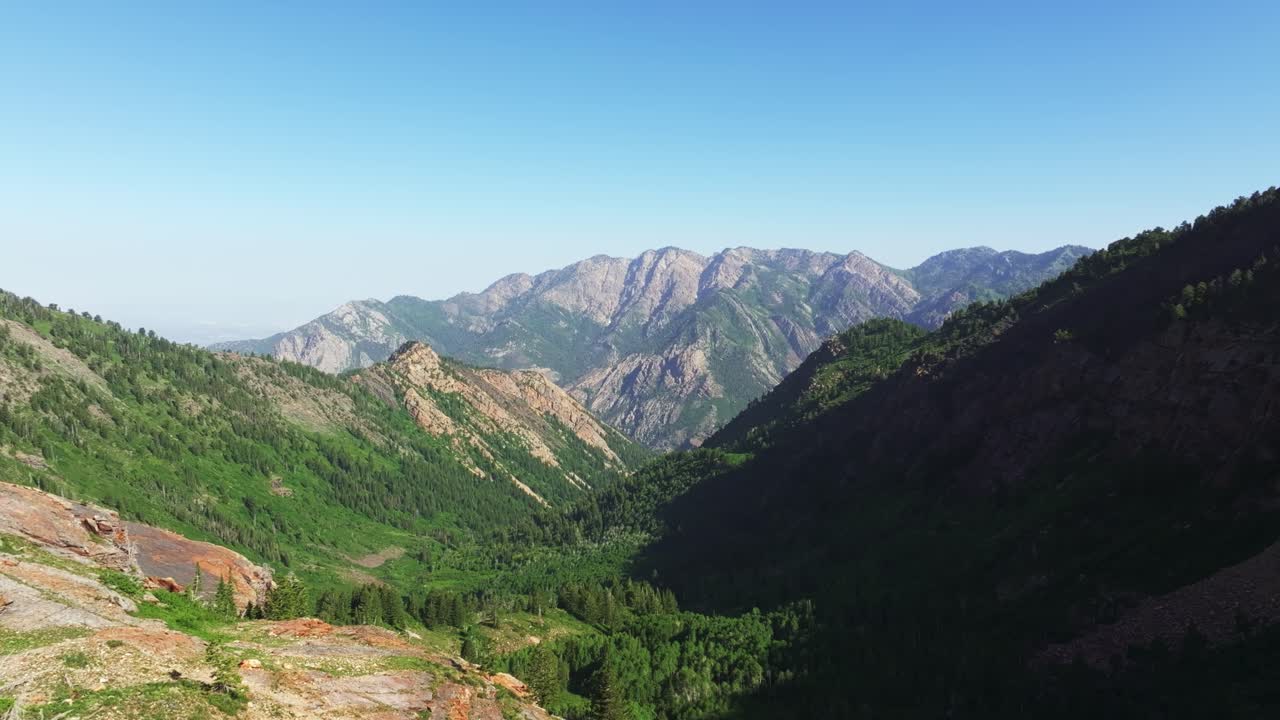 Aerial drone shot of Mount Raymond and Gobbler’s Knob in Big Cottonwood Canyon near Salt Lake City, Utah, on a clear summer morning with lush green foliage and pine trees along the Lake Blanche trail