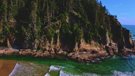 Aerial-flying-forward-rising-over-beach,-waves,-revealing-ocean-cliffs,-trees