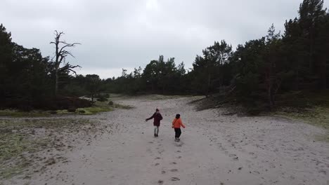 drone shot of two people in bright jackets running through a sandy desert forest savanna