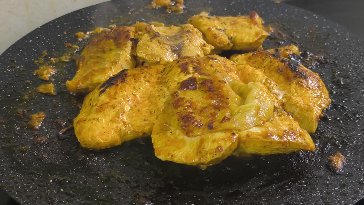Chicken meat, marinated with spices, is grilled on a flat, non-stick pan. The spices sizzle, releasing a delicious aroma. Close-up shot shows the chicken browning perfectly on the grill