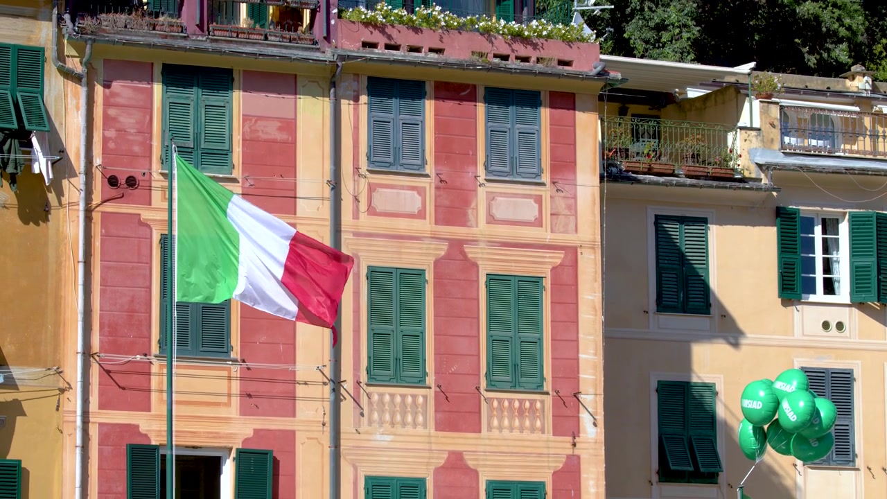 Statisch beeld van een nationale vlag die wappert tegen een levendig Mediterraan gebouw met groene luiken.