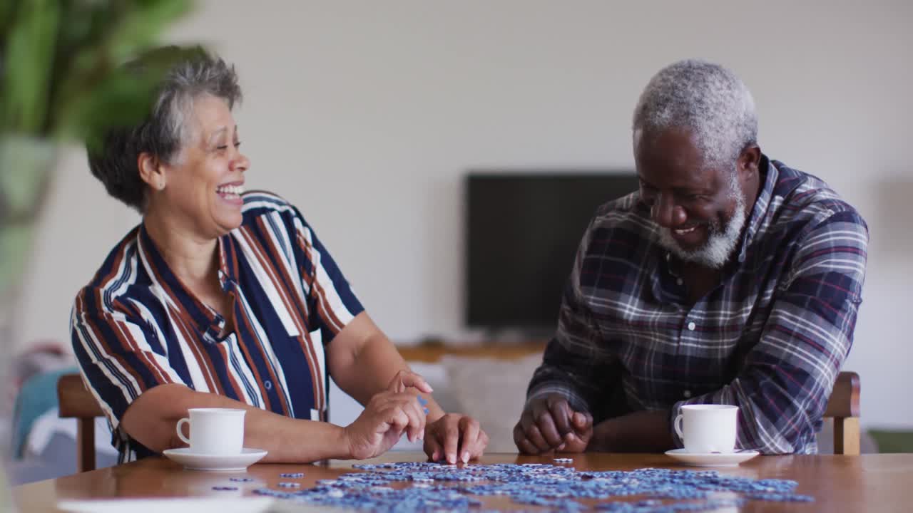 una pareja de ancianos afroamericanos sentados a la mesa haciendo rompecabezas bebiendo té