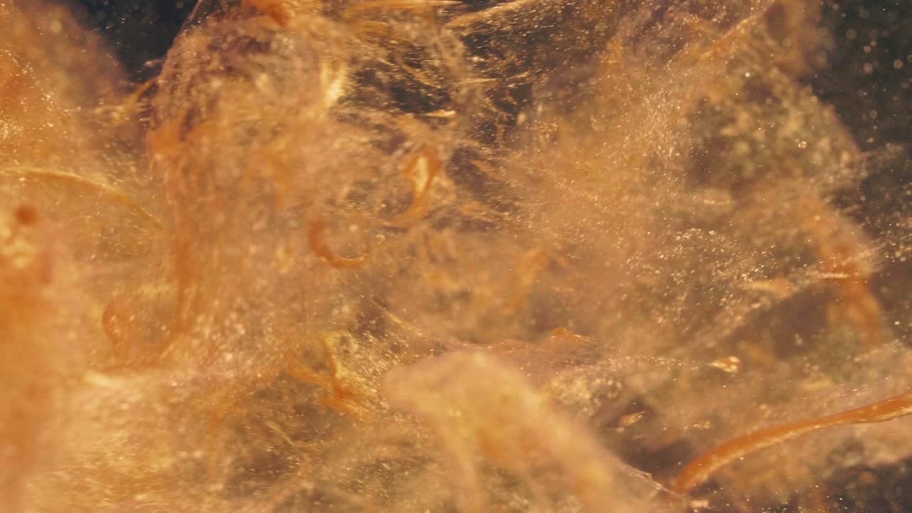 황금 잉크 입자는 검은 바탕에 다채로운 혼란으로 물에 흐른다.