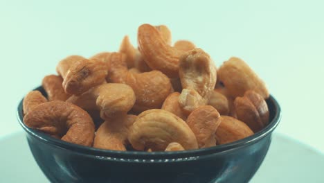 A-close-up-shot-of-a-roasted-salty-cashew-in-a-black-shiny-bawl-on-a-rotating-stand,-slow-motion,-4k,-Tasty