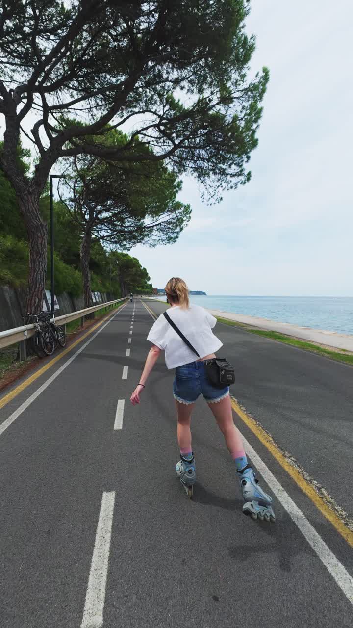 Vertical of blonde woman rollerblading on scenic coastal path. Rear follow cam