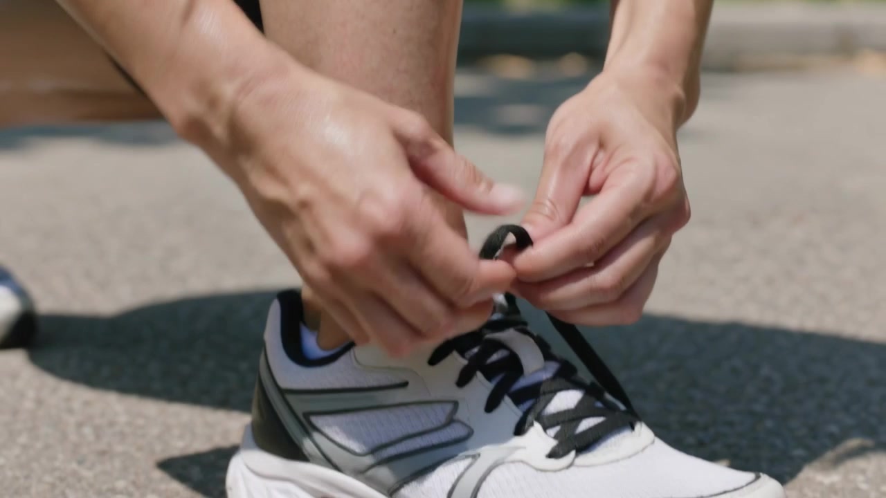 Mulher aquecendo, curvando-se para amarrar cadarços pretos em tênis de corrida em um caminho no parque, vestindo shorts pretos