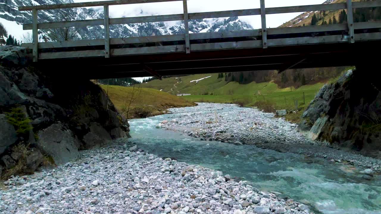 un dron aéreo cercano vuela a través del vuelo debajo de un puente en el pintoresco valle de ahornboden engtal a lo largo del río de montaña rissach en los alpes bávaros austríacos en un día nublado y soleado en la naturaleza