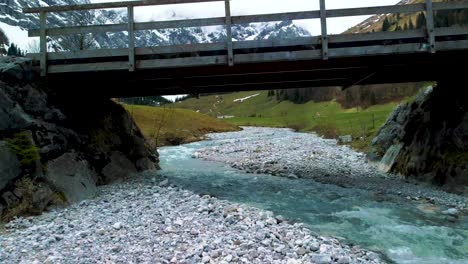 close low aerial drone fly through flight below a bridge at scenic ahornboden engtal valley along rissach mountain river in the bavarian austrian alps on a cloudy and sunny day in nature